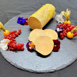 ballottine de foie gras de canard fait maison traiteur mis en valeur sur planche d'ardoise avec des fleurs comestibles et fruits rouges
