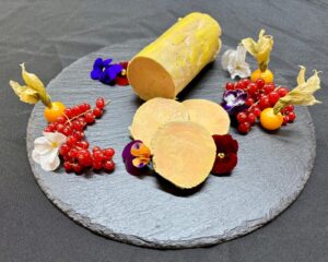 ballottine de foie gras de canard fait maison traiteur mis en valeur sur planche d'ardoise avec des fleurs comestibles et fruits rouges